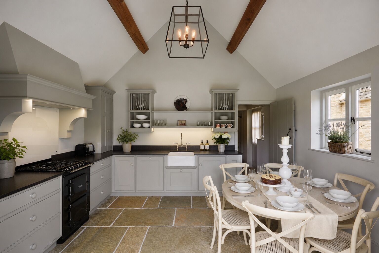 A kitchen with a dining area, featuring a stove, sink, and white cabinets.