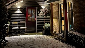 Een bakstenen huis met een rode deur, een trap naar een overdekte veranda en een met sneeuw bedekte grond.