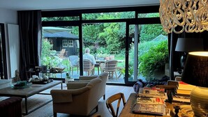 Een moderne woonkamer met een eettafel, stoelen en een uitzicht op de tuin door grote ramen.
