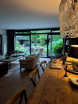 Ein modernes Wohnzimmer mit einem Esstisch, Stühlen und Blick auf den Garten durch große Fenster.