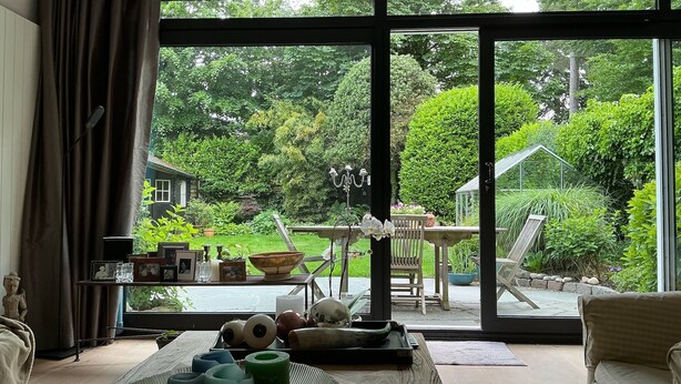 Een kamer met een grote schuifdeur naar een tuin, een tafel met decoratieve voorwerpen, en een bank.