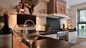 Een moderne keuken met een wijnfles en glazen, een fornuis en een raam met jaloezieën.