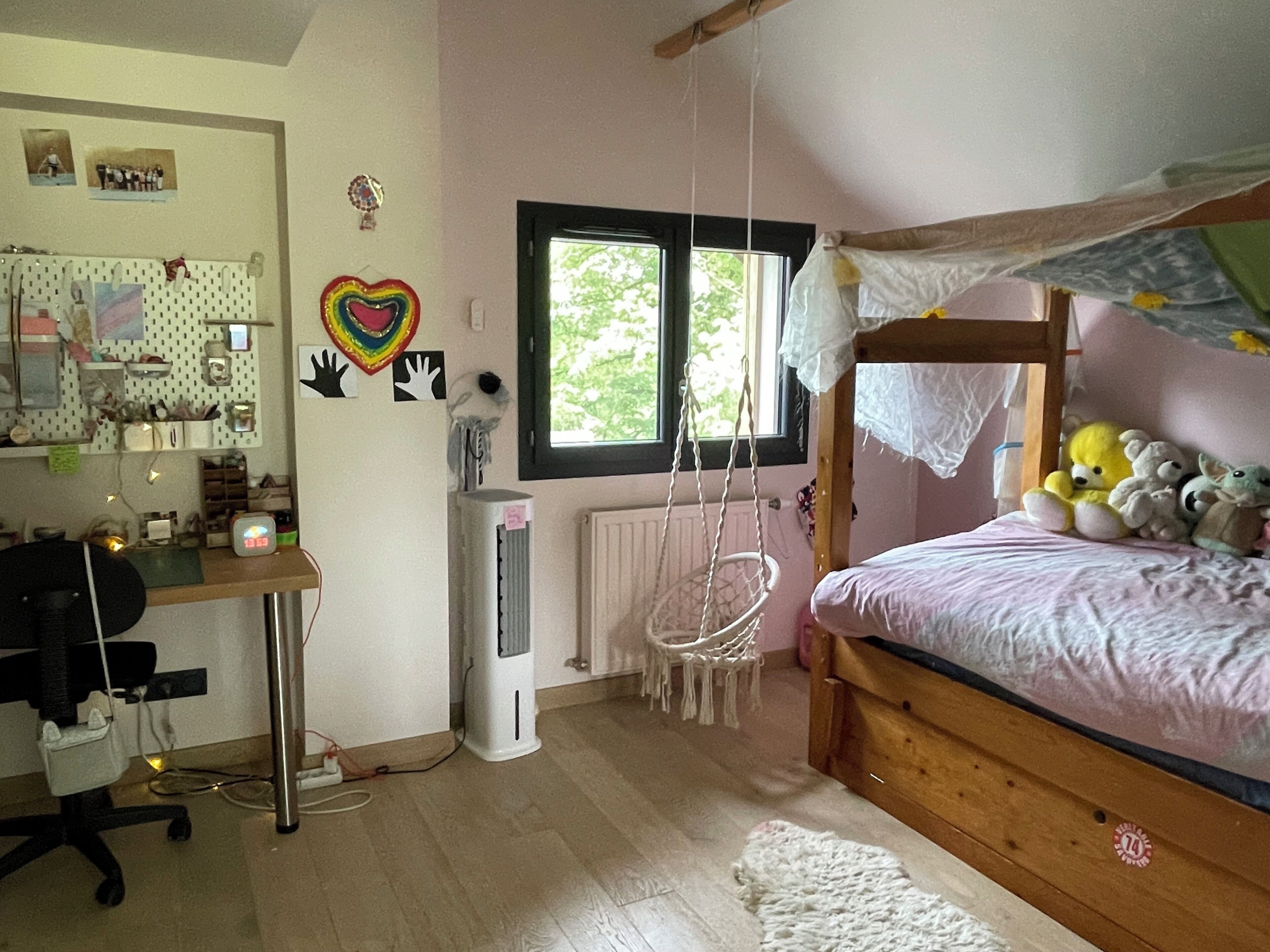 Une chambre avec un lit superposé, un bureau avec une chaise, un fauteuil suspendu et un radiateur.