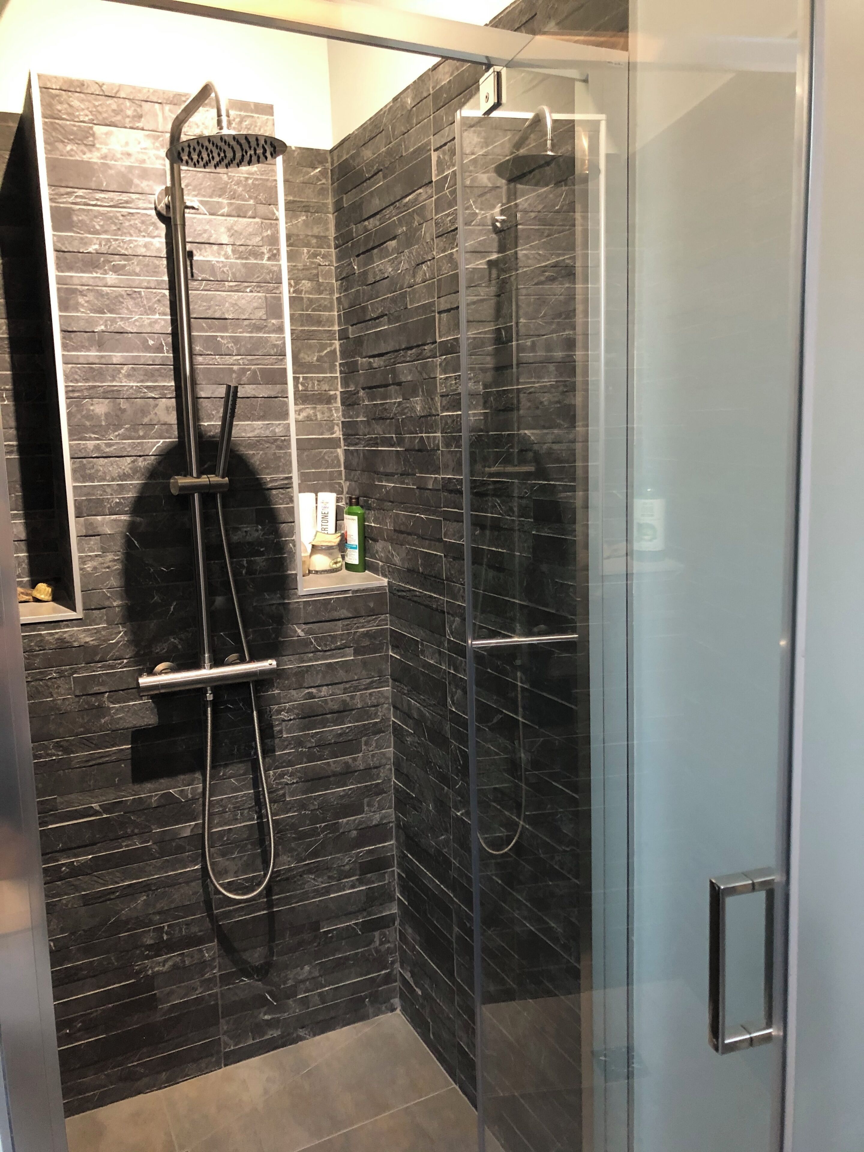 A modern bathroom with a glass shower enclosure, a handheld showerhead, and a wall-mounted towel rack.
