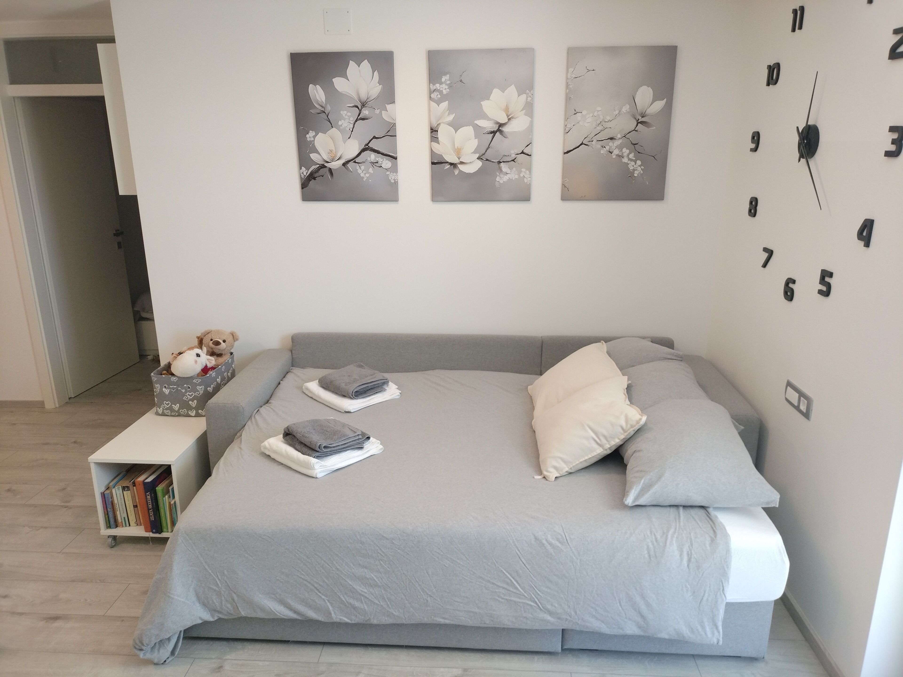 A bedroom with a bed, pillows, a nightstand, a bookshelf, and wall art.