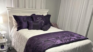 Ein ordentlich bezogenes Bett mit einem weißen Kopfteil, einer violetten Bettdecke und passenden Kissen.