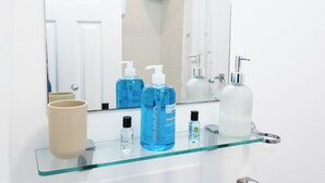 A bathroom with a glass shelf holding toiletries, a mirror, and a shower area. - Bayview Aparthotel by Guestz (Morecambe)
