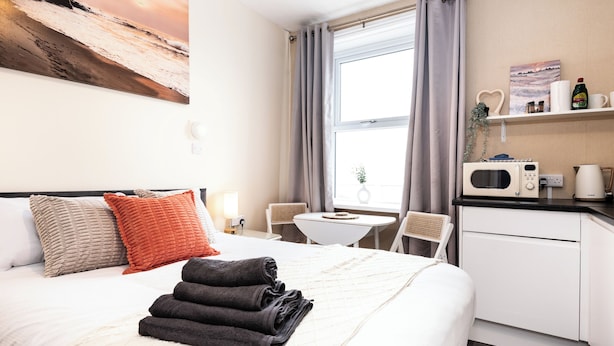A hotel room with a bed, a desk, a microwave, a coffee maker, and a window with curtains. - Bayview Aparthotel by Guestz (Morecambe)