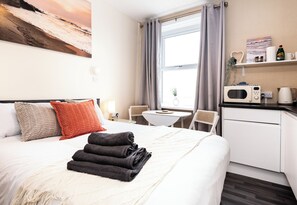 A hotel room with a bed, a desk, a microwave, a coffee maker, and a window with curtains. - Bayview Aparthotel by Guestz (Morecambe)