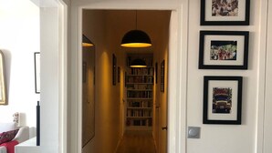 Een gang met een houten vloer, een boekenkast en ingelijste foto’s aan de muur.