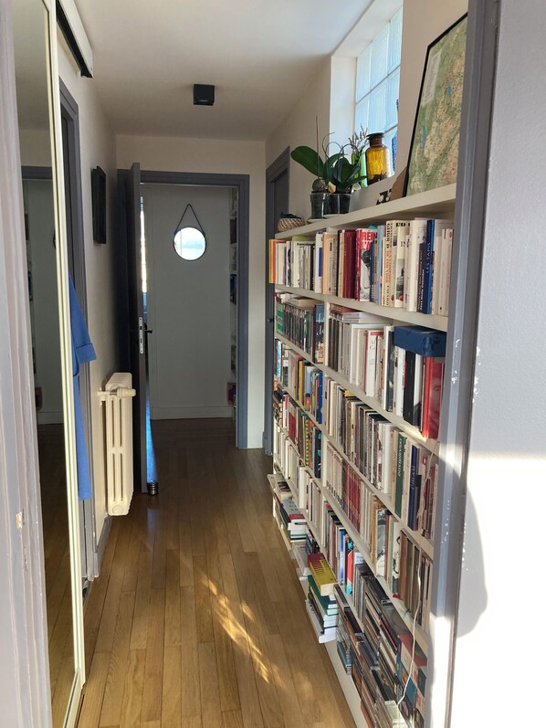 A hallway with a bookshelf filled with books, a radiator, and a door leading to another room. - Very Cosy Family appartment in Paris, 5 min walk to Eiffel Tower & Invalides (Paris)
