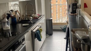 Een moderne keuken met witte kasten, een zwart aanrecht en uitzicht op gebouwen door een raam.