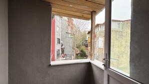 Habitación de esquina con ventana que da a una zona residencial, techo de madera y pared con textura.