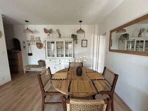Ein Esszimmer mit einem Holztisch, gewobenen Stühlen, einem weißen Schrank und hängenden Pendelleuchten.
