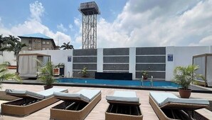 A rooftop pool area with lounge chairs and a view of a building with a blue roof. - GOLDLIZ APARTMENT (Abuja)
