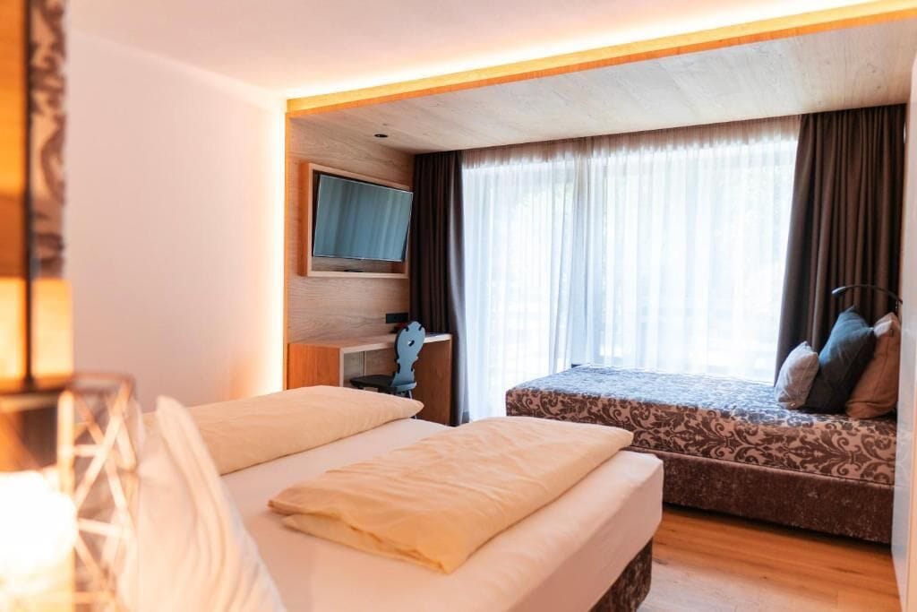 A hotel room with a bed, a desk, a television, and a window with curtains.