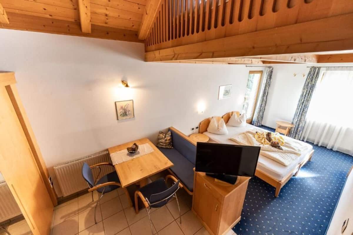 A room with a bed, a desk with a chair, a television, and a window.