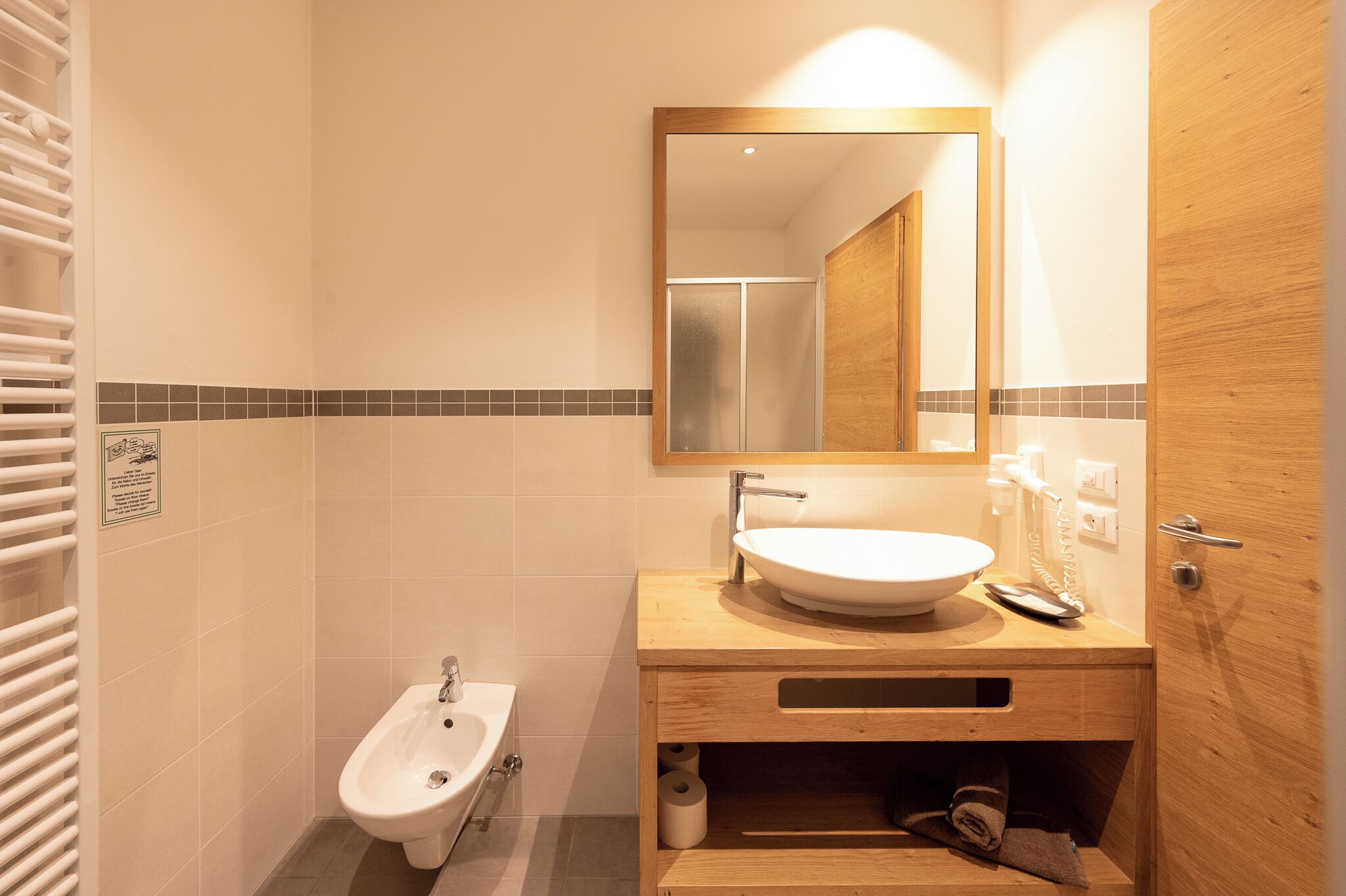 A bathroom with a white sink, a bidet, a mirror, and a wooden vanity.
