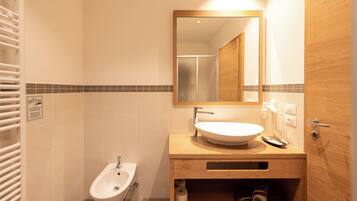 A bathroom with a white sink, a bidet, a mirror, and a wooden vanity.