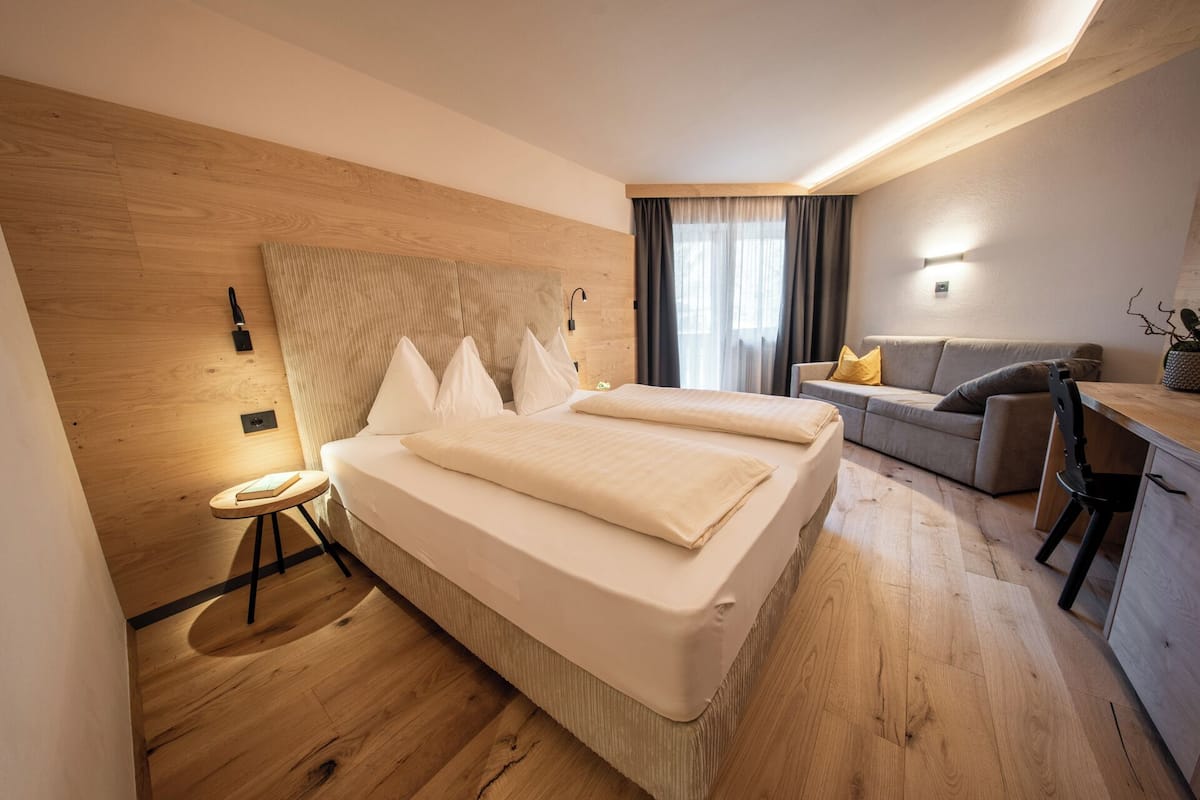 A modern hotel room with a large bed, a desk, a sofa, and a small table.