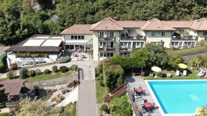 A multi-story hotel with a swimming pool, outdoor seating, and a view of a forested hillside.