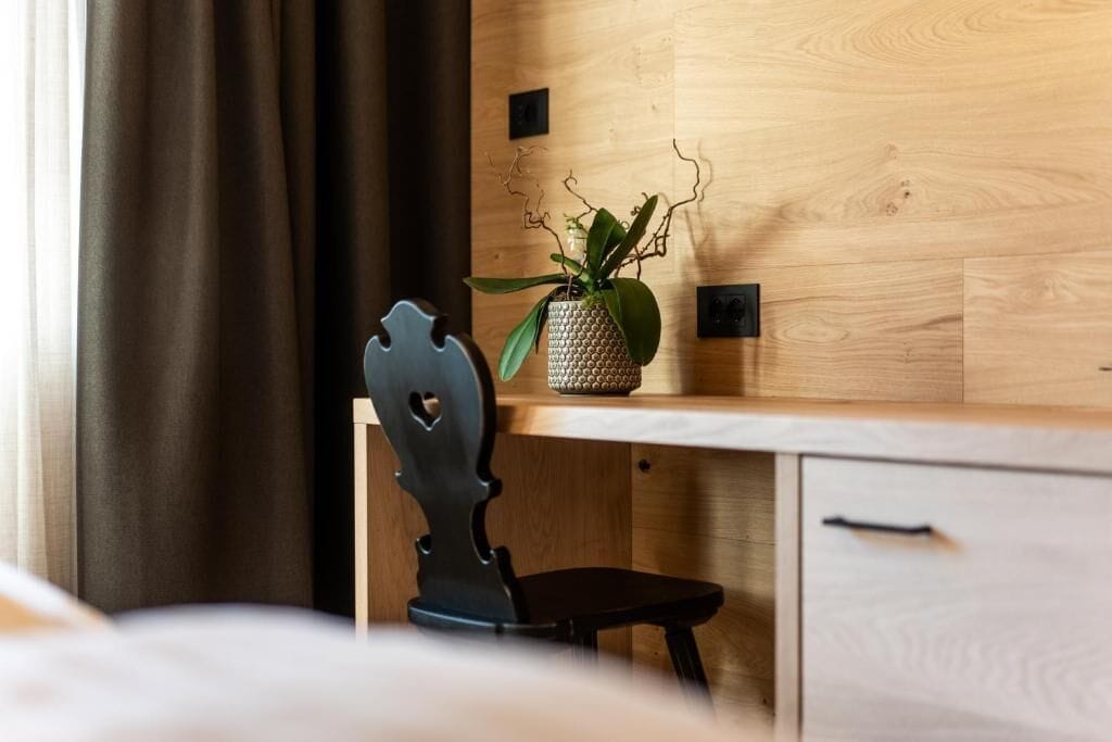A hotel room with a wooden desk, a chair, a potted plant, and a bed.