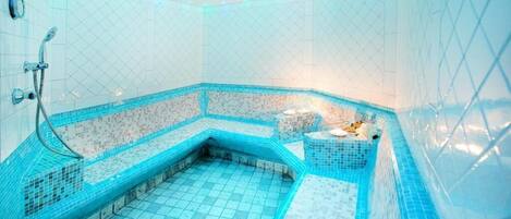 Un baño con ducha en esquina, paredes con azulejos y una pequeña zona de estar.