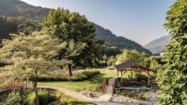 A garden with a wooden bridge, a gazebo, and a pond.
