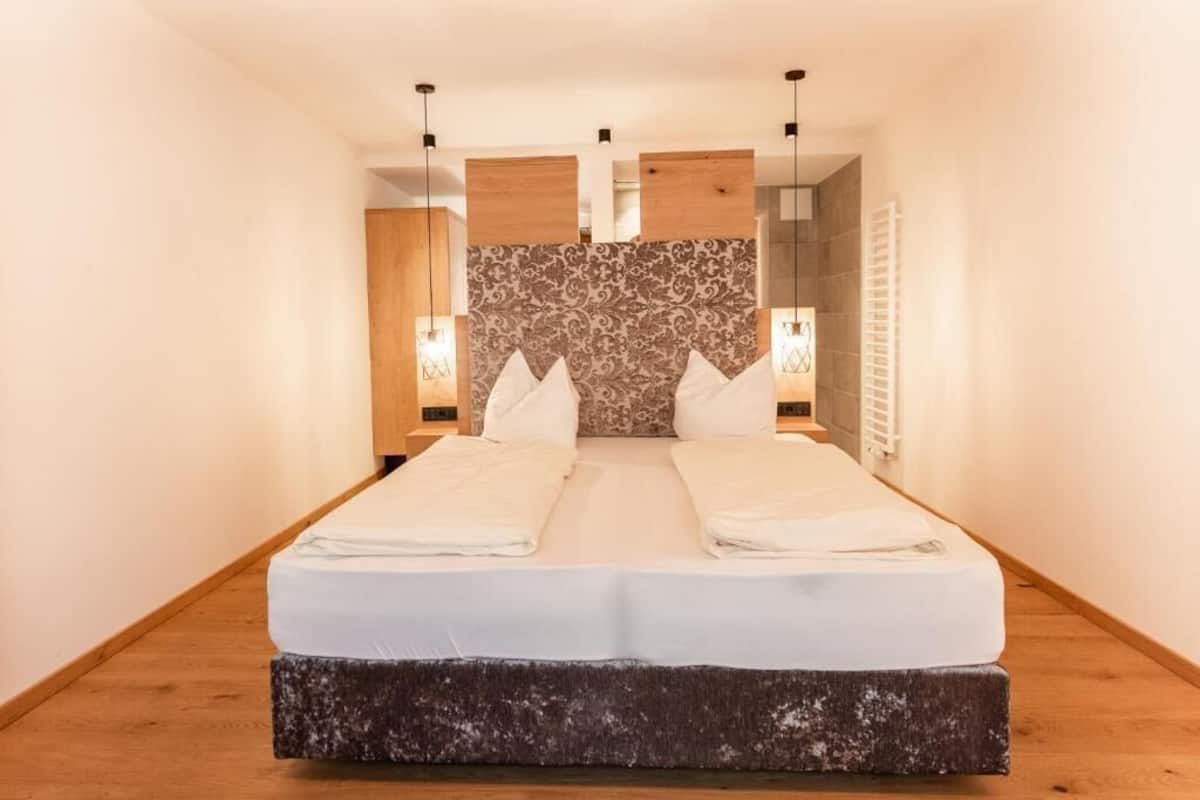 A hotel room with a large bed, wooden headboard, bedside lamps, and a wooden floor.