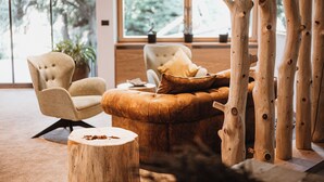 A modern living room with a tufted armchair, a leather ottoman, a round wooden table, and a large window with natural light.