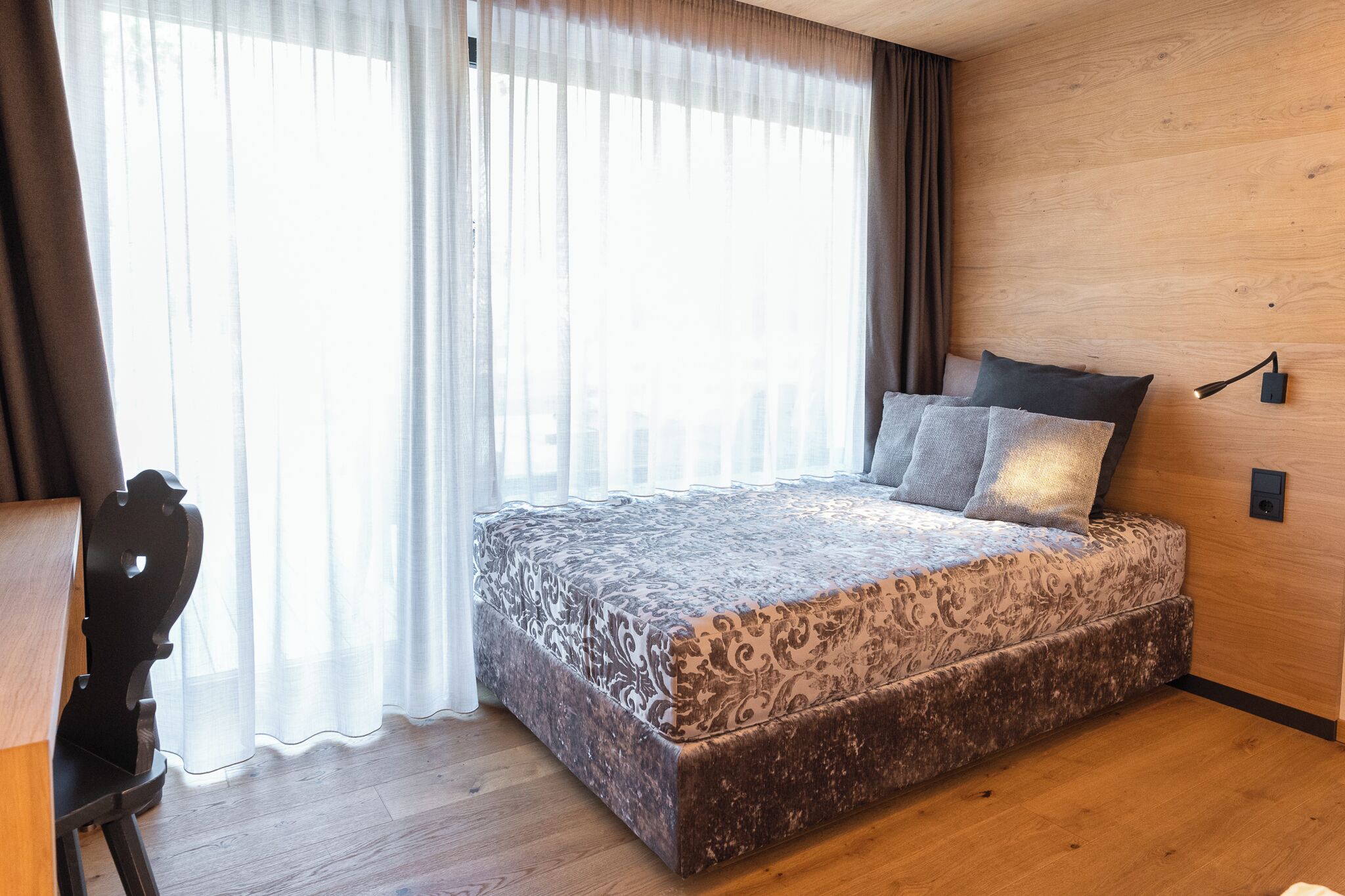 Quarto com cama grande, paredes de madeira, escrivaninha e cadeira.