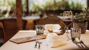 A table set with cutlery, a wine glass, a small glass, and a wooden board with a ring.