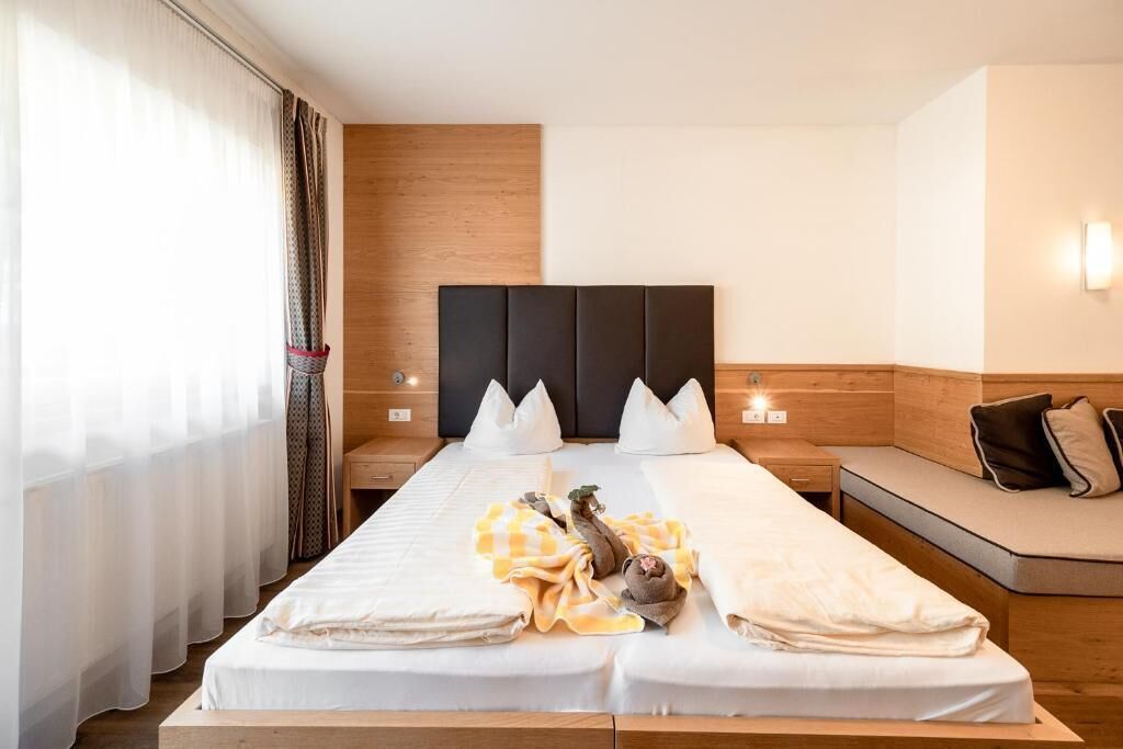 Una habitación de hotel con una cama grande, mesitas de noche, cabecera de madera y un banco junto a la ventana.