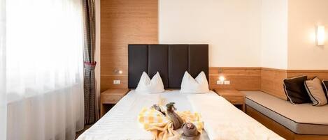 Una habitación de hotel con una cama grande, mesitas de noche, cabecera de madera y un banco junto a la ventana.