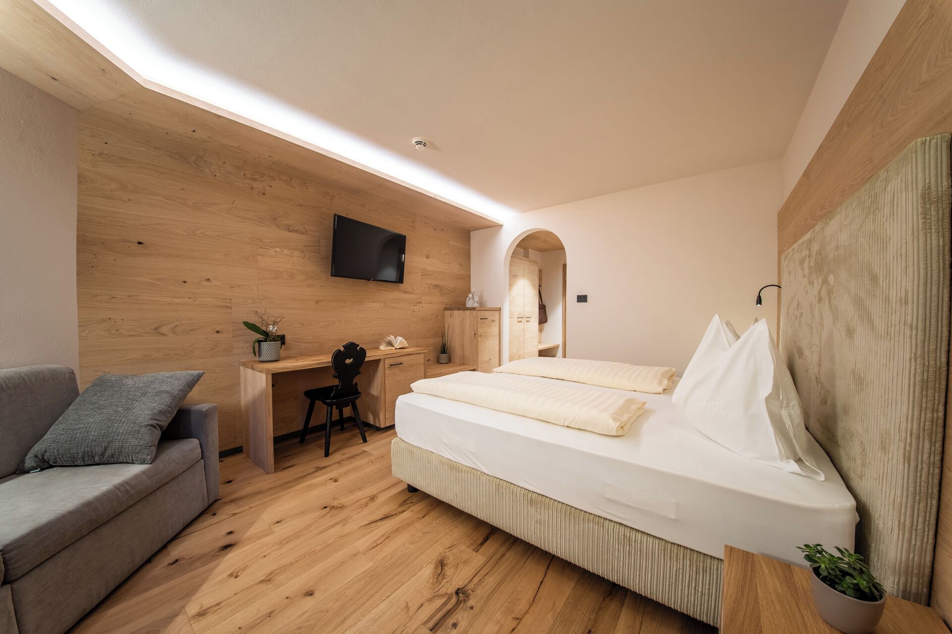 A modern bedroom with a wooden ceiling, a bed, a desk, a chair, and a television.