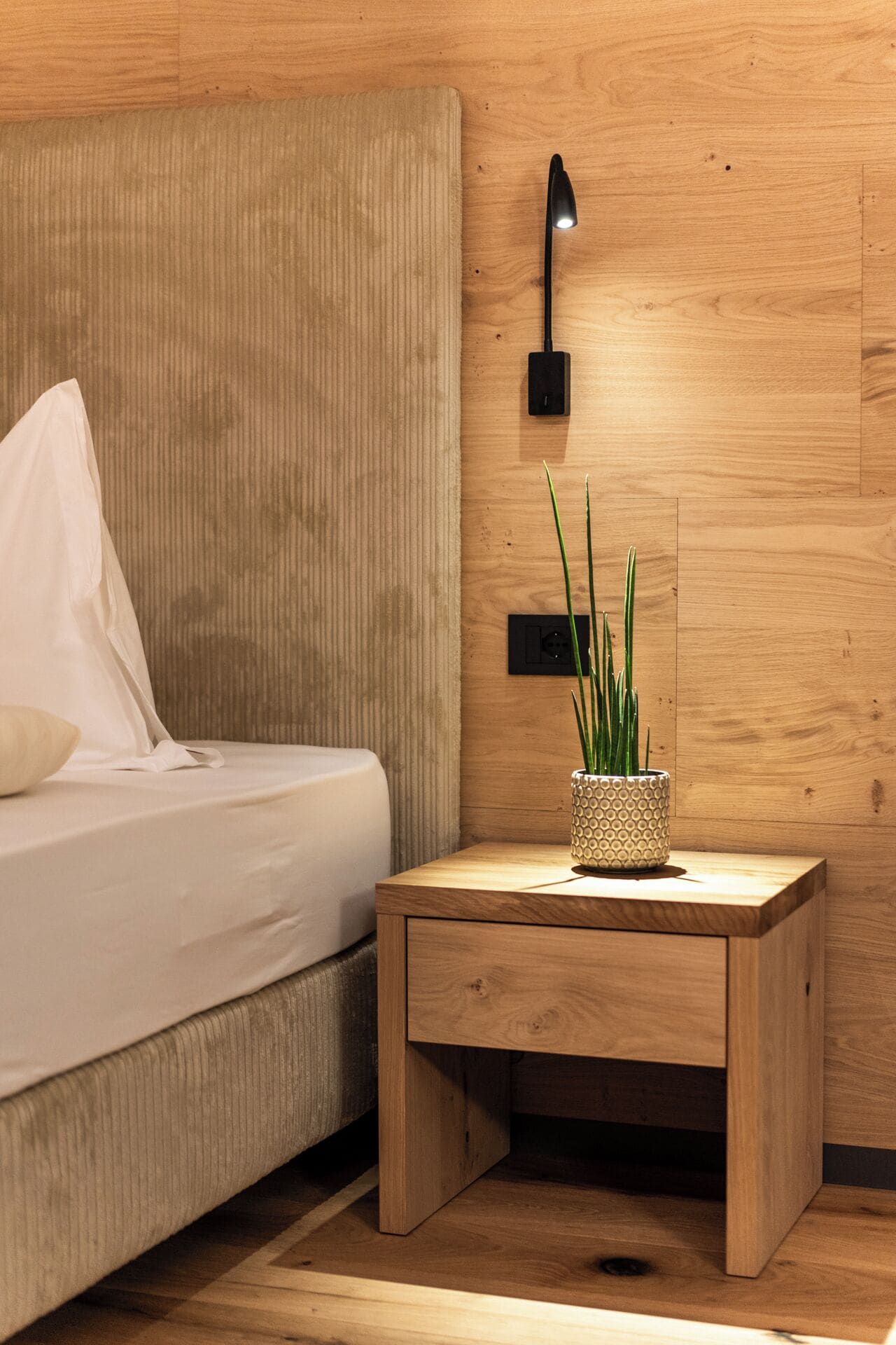 A bedroom with a bed, bedside table, lamp, and a potted plant.