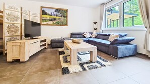 Uma sala de estar com televisão, sofá, mesa de centro e um quadro na parede.