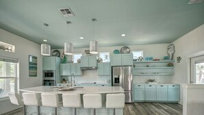 A modern kitchen with a central island, bar stools, light blue cabinets, stainless steel appliances, and pendant lighting. - No Plana Cabana Close to Beach (Port Aransas)