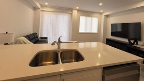 Une cuisine moderne dotée d’un grand îlot central, d’un évier à deux bacs et d’un téléviseur à écran plat fixé au mur.