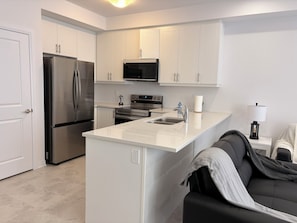 A modern kitchen with white cabinets, stainless steel appliances, a central island, and a black leather couch.