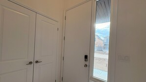 Un couloir avec deux portes blanches et une porte en verre donnant sur l’extérieur.