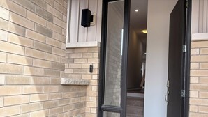 Une porte d’entrée avec une porte en verre, un mur de briques et une petite étagère sur laquelle se trouve un objet noir.
