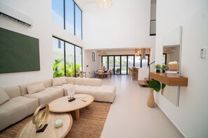 A modern living room with a sectional sofa, a round coffee table, and a dining area with natural light. - Villa de lujo totalmente equipada en Vista Cana a minutos del centro (Punta Cana)