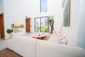 A modern living room with a large sofa, a coffee table, and a view through a glass door to a balcony. - Villa de lujo totalmente equipada en Vista Cana a minutos del centro (Punta Cana)