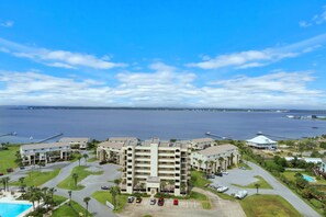 A multi-story hotel with a central courtyard, parking area, and a view of the sea. - Santa Rosa Towers Unit 1402 (Pensacola Beach)