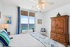 Ein Schlafzimmer mit Bett, einem Holzschrank, einem Sessel und einem Balkon mit Meerblick.