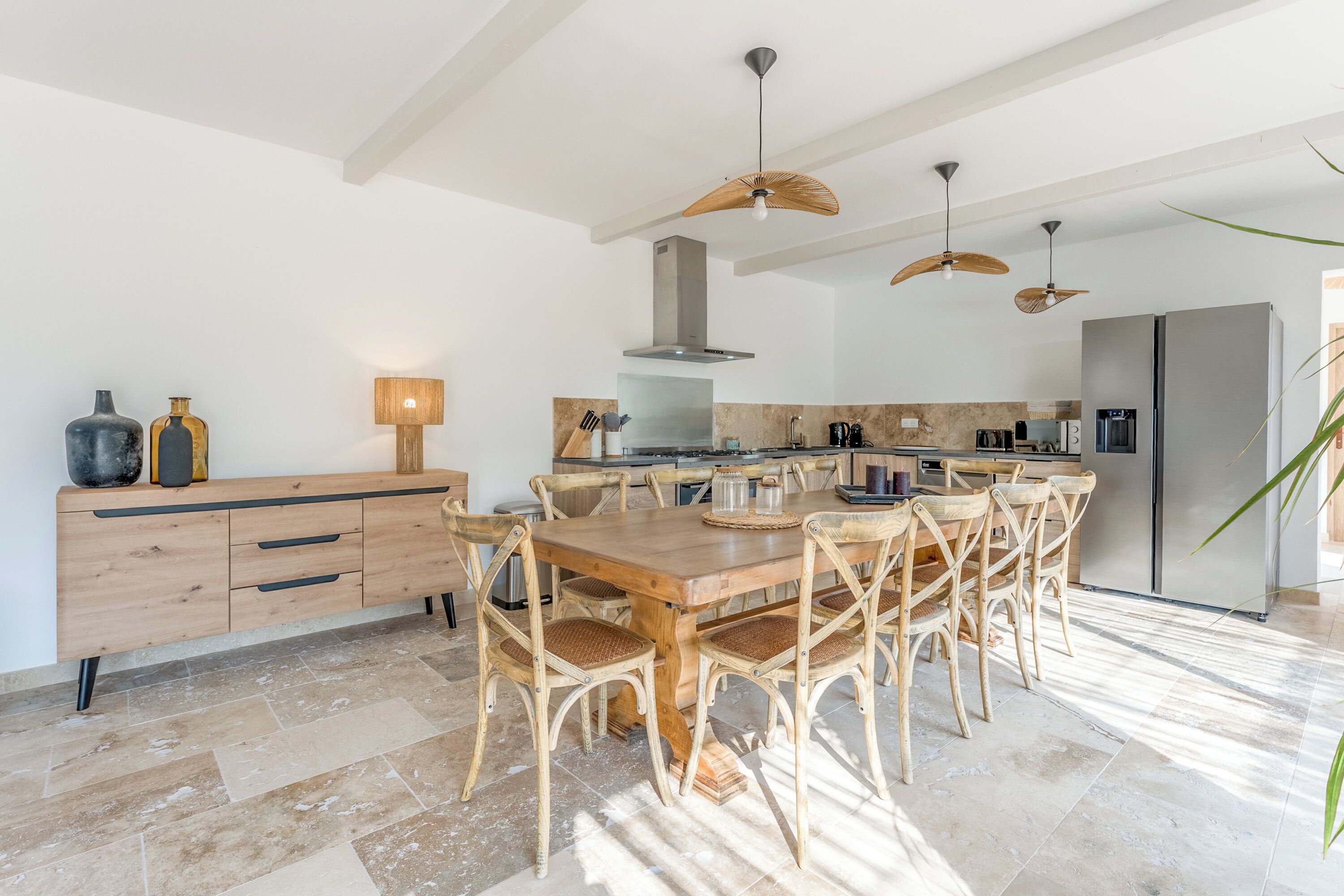 A modern kitchen with a wooden dining table, wicker chairs, and a stainless steel refrigerator.