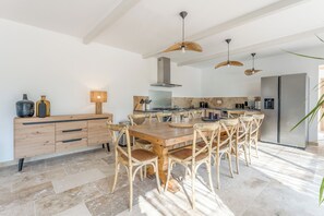 A modern kitchen with a wooden dining table, wicker chairs, and a stainless steel refrigerator.