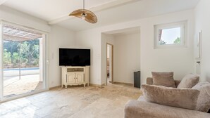 Un soggiorno con televisione a schermo piatto su un mobile bianco, divani color beige, una grande finestra e una porta che dà sull'esterno.