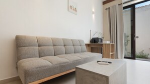 A modern living room with a sofa, a coffee table, a TV, and a sliding glass door leading to an outdoor area. - Artemis Studio Apartment in Laganas, Zante with Sea Activities (Laganas)